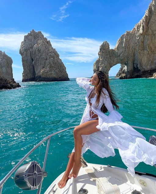 Wanita memakai beachwear hijau stylish di tepi laut dengan latar batu karang dan langit biru cerah