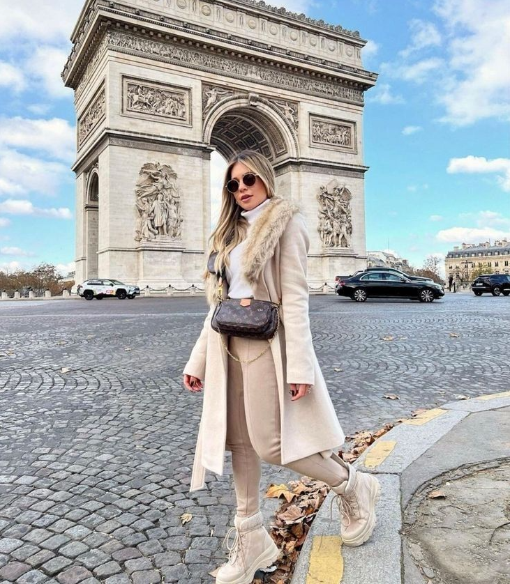 Wanita stylish mengenakan winter outfit streetstyle 2025 dengan coat panjang di depan Arc de Triomphe Paris